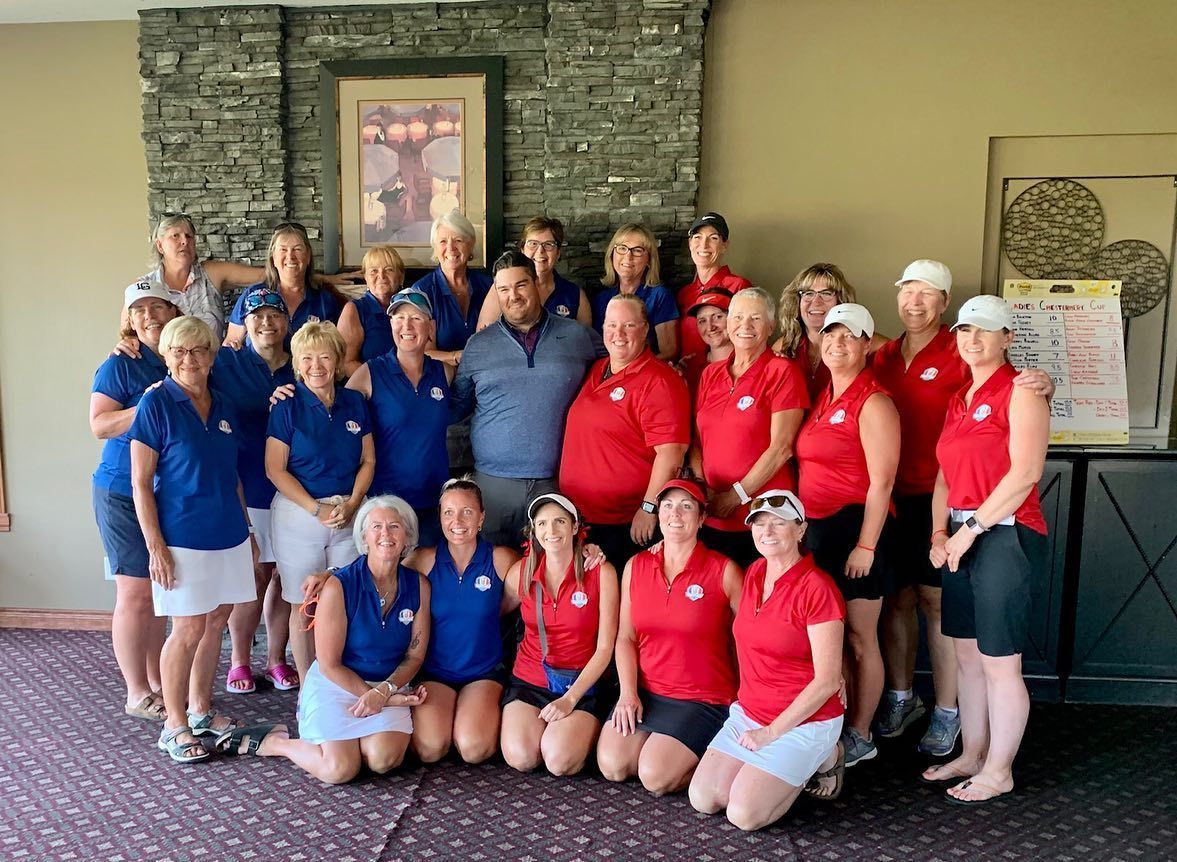 Group of people in red and blue shirts posing near a stone wall, likely after a golf event.