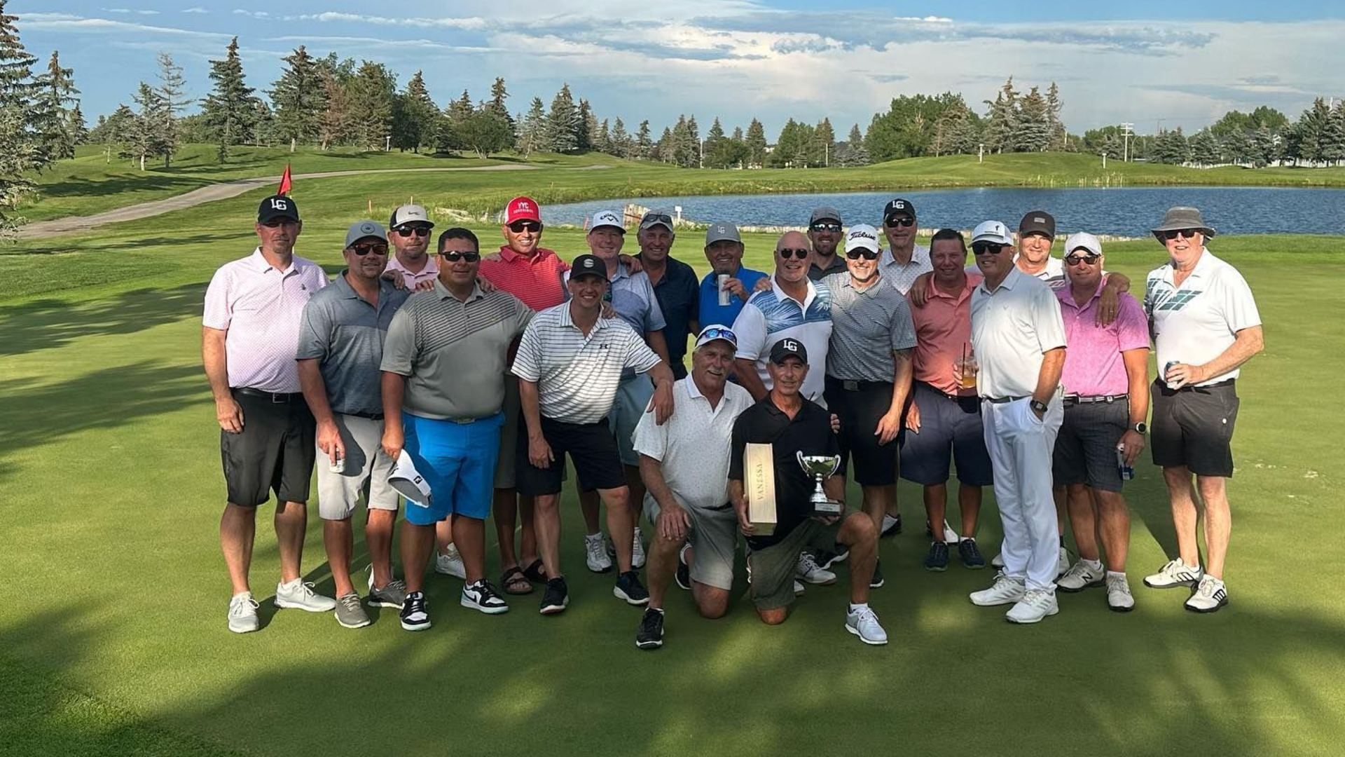 Group of men pose on golf course, holding a trophy.