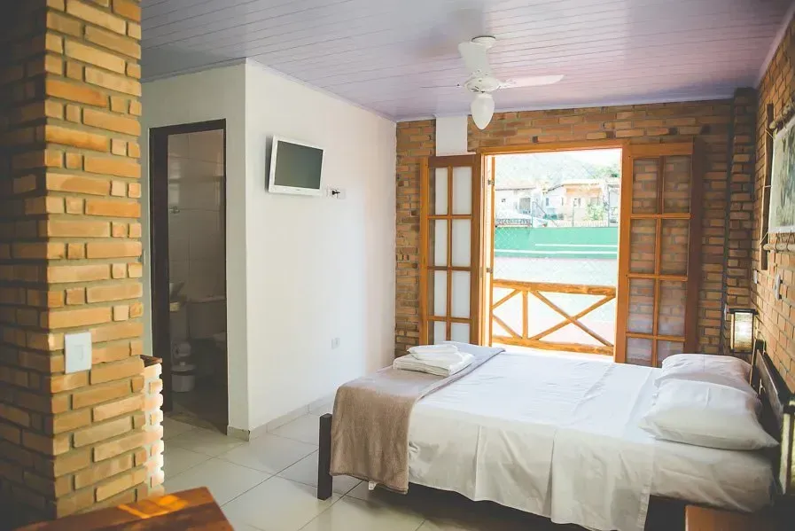 Um quarto com uma cama, televisão e uma parede de tijolos.
