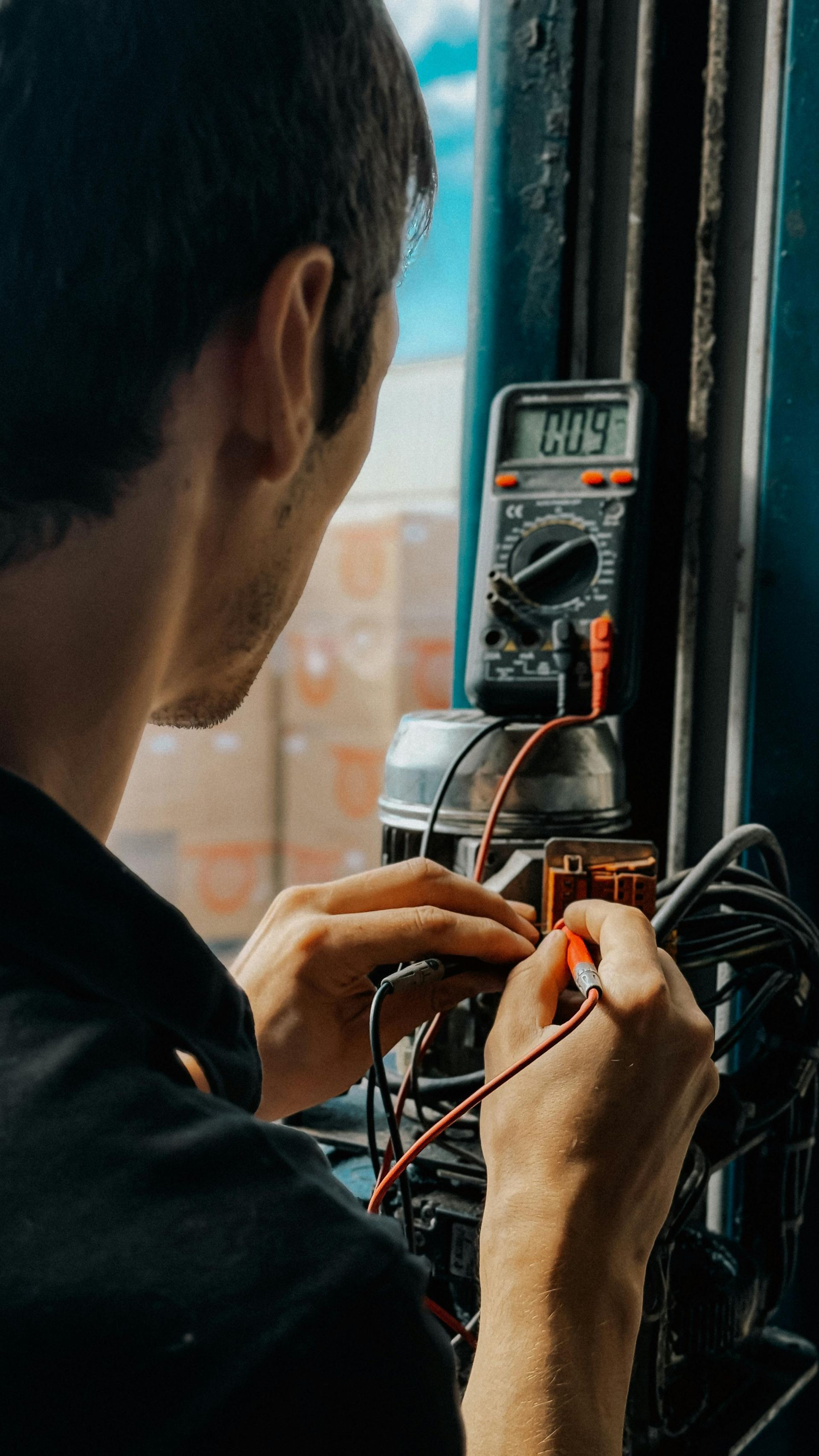 Person using a multimeter to inspect electrical wiring near a window.