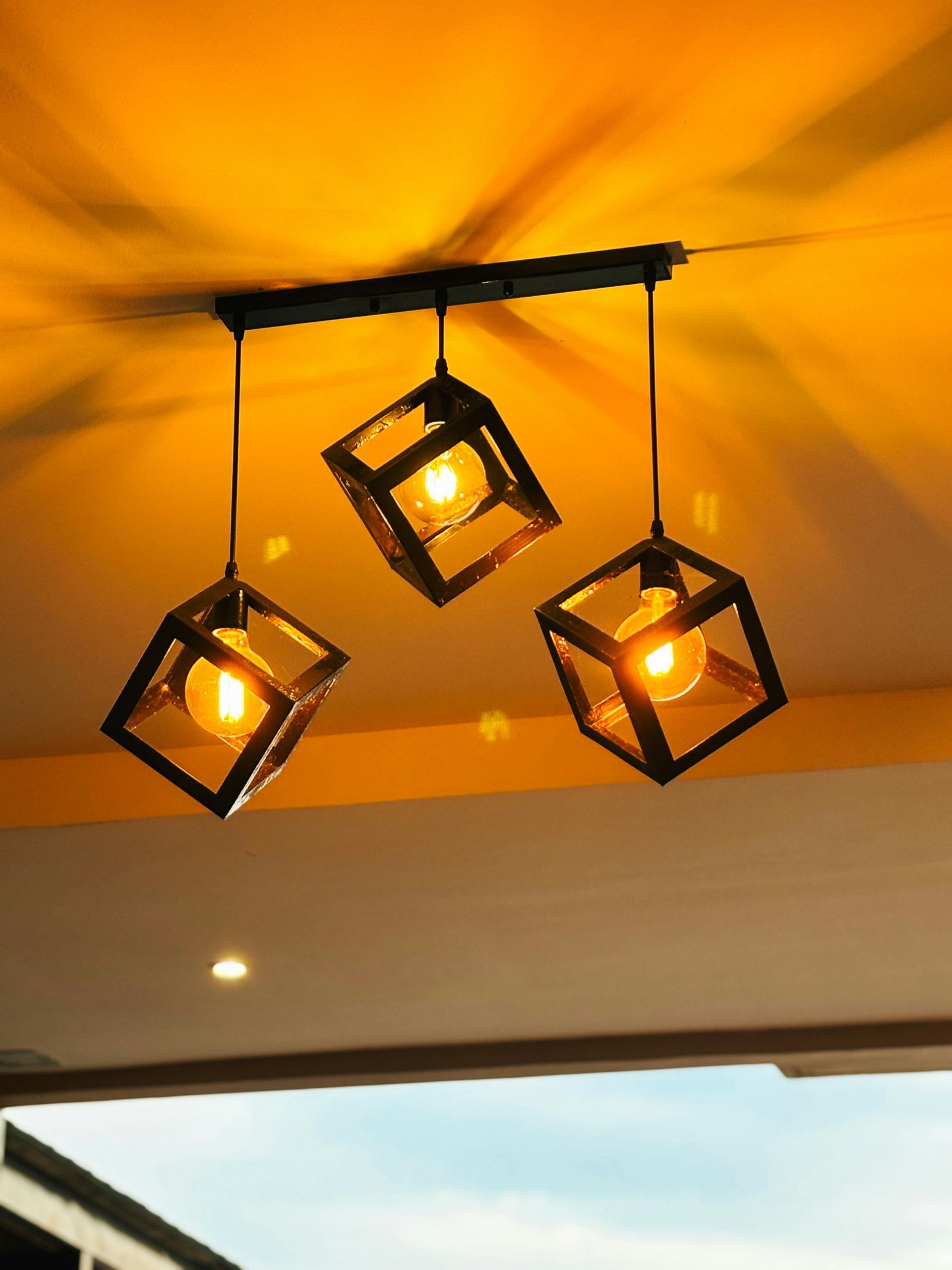 Three hanging black cube lights with warm bulbs on a yellow ceiling