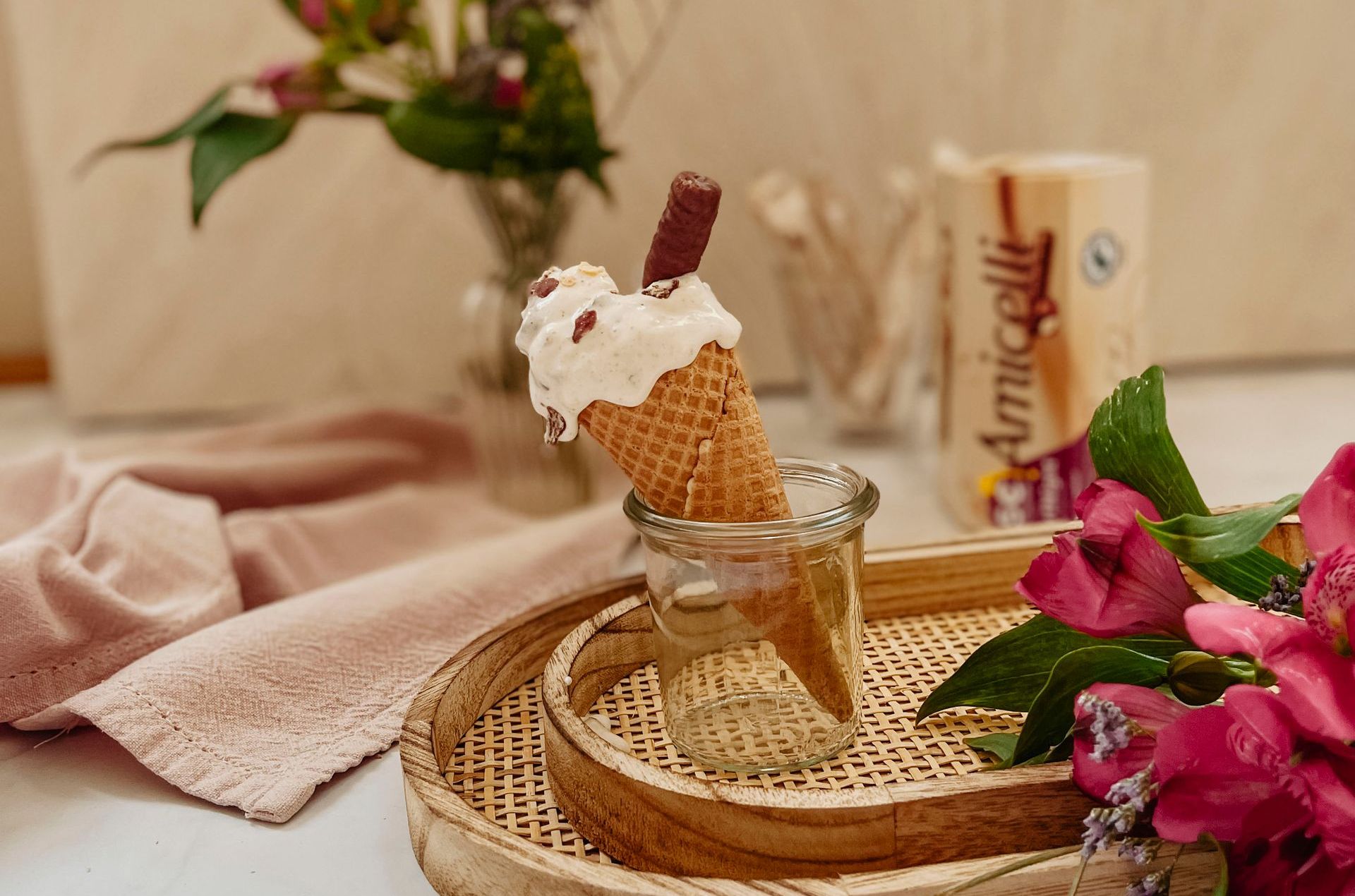An ice cream cone is sitting on a wooden tray next to flowers
