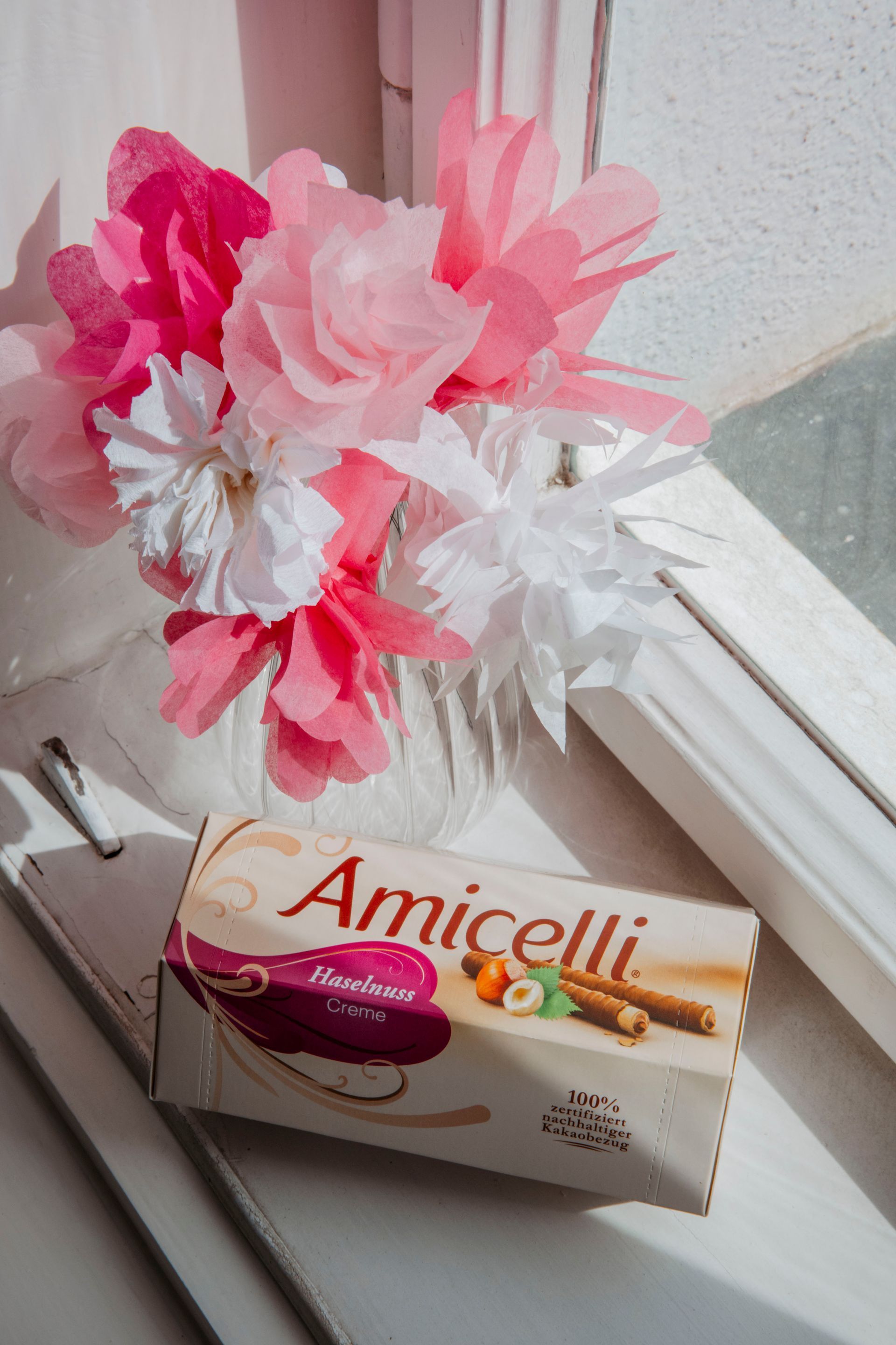 A box of amicielli sits on a window sill next to a vase of flowers