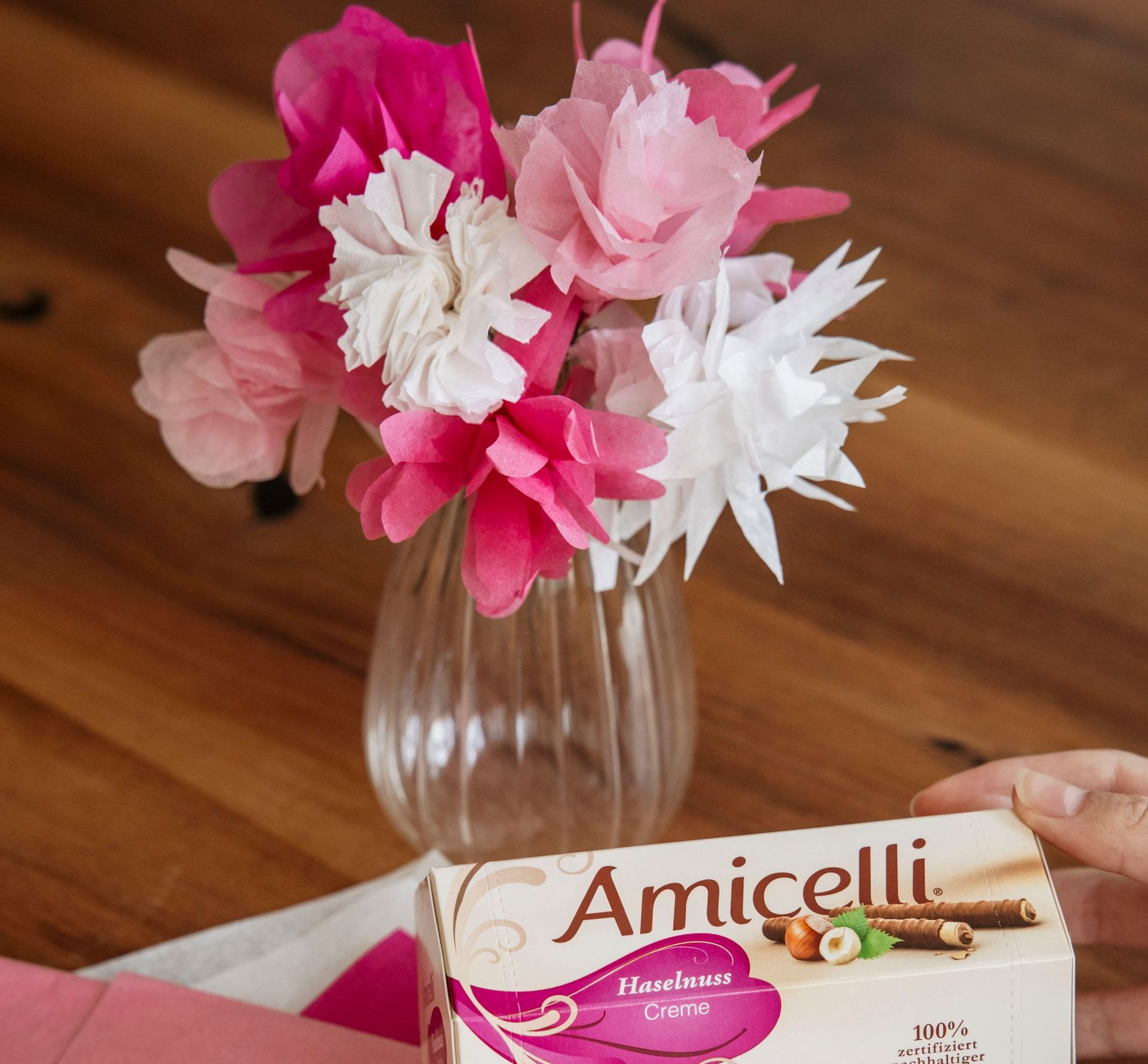 A box of amicielli sits on a table next to a vase of paper flowers