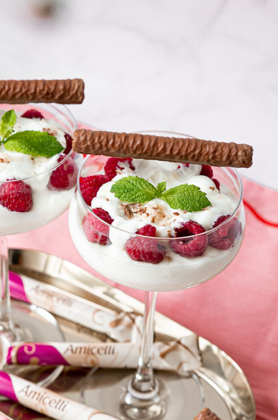 Two glasses of raspberry dessert, topped with mint and chocolate wafer, on a silver tray.