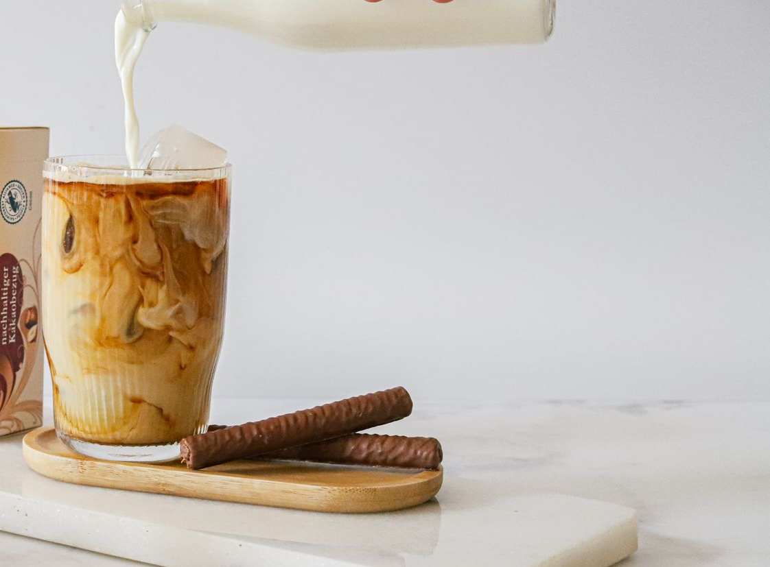 A person is pouring milk into a cup of iced coffee with amicelli.