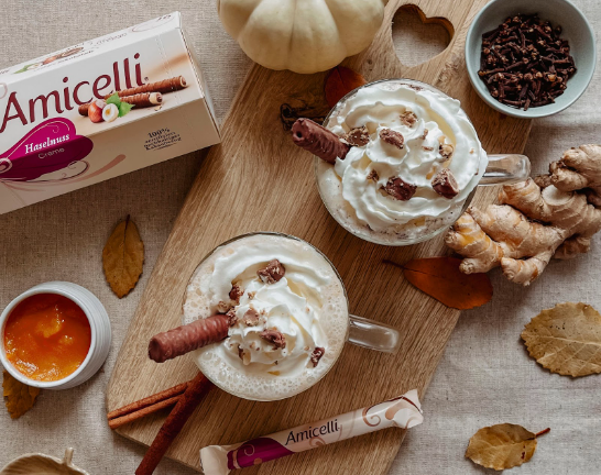 Two cups of hot chocolate with whipped cream and cinnamon sticks on a wooden cutting board