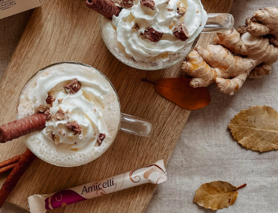 Two cups of hot chocolate with whipped cream and cinnamon sticks on a wooden cutting board