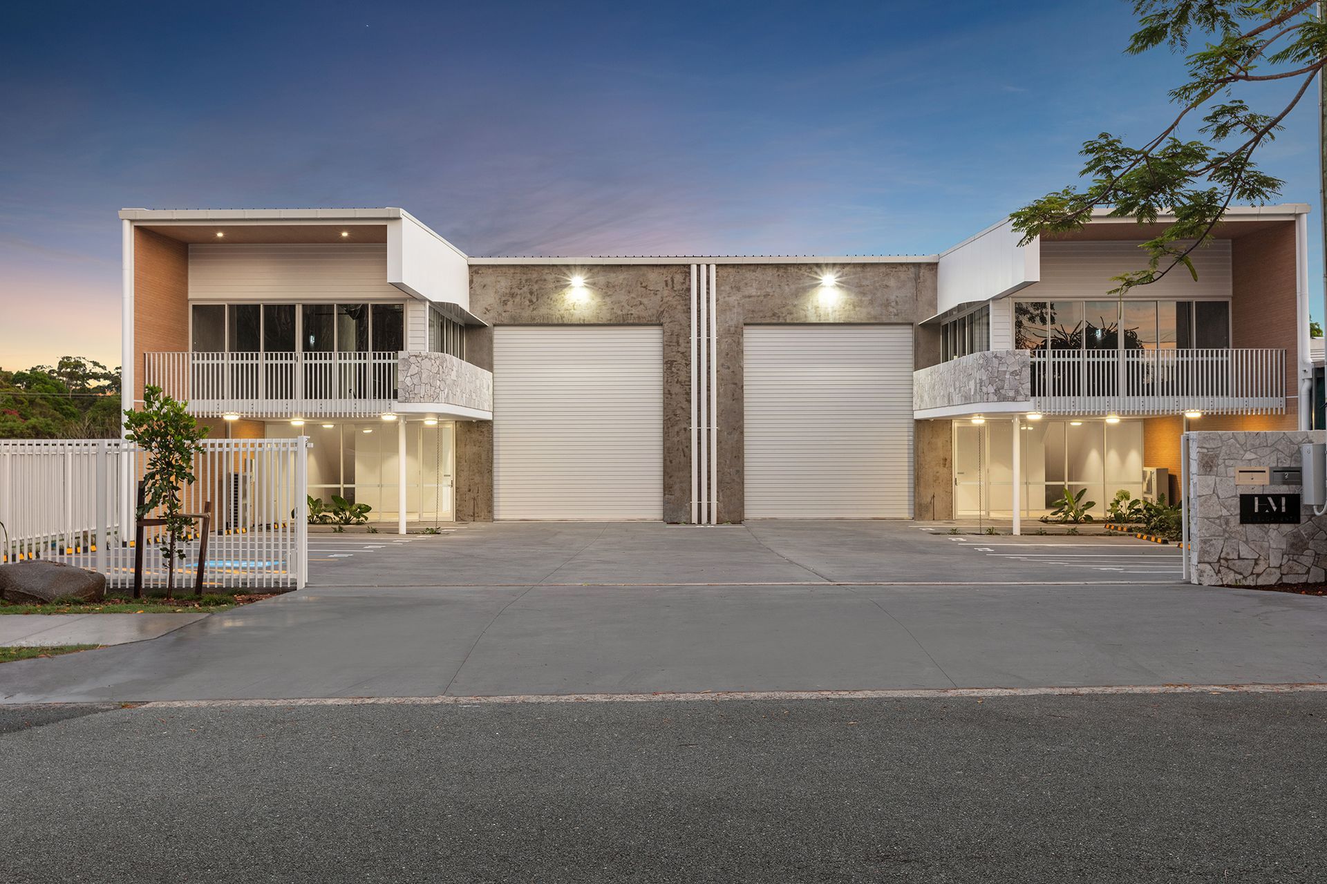 A modern industrial building with dual roll-up doors, glass office facades, and light stone exterior walls at dusk.