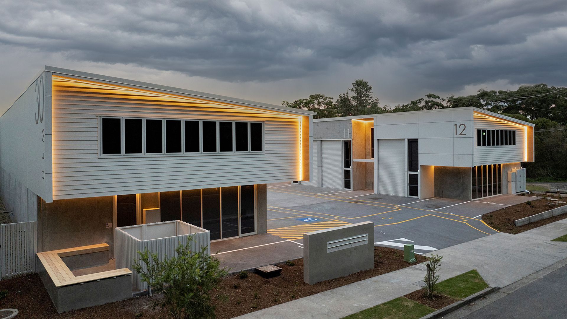 Modern, two-story white commercial buildings with strip lighting, large windows, and a paved parking lot at dusk.
