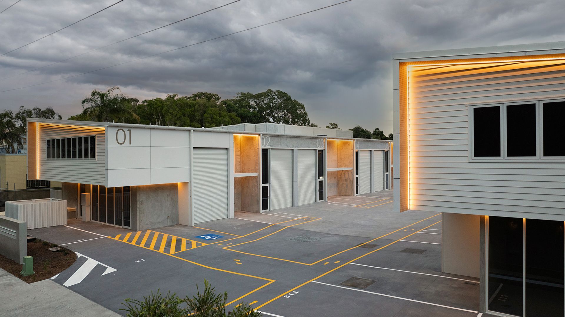 Modern white industrial warehouse complex with parking spaces under an overcast sky at twilight.