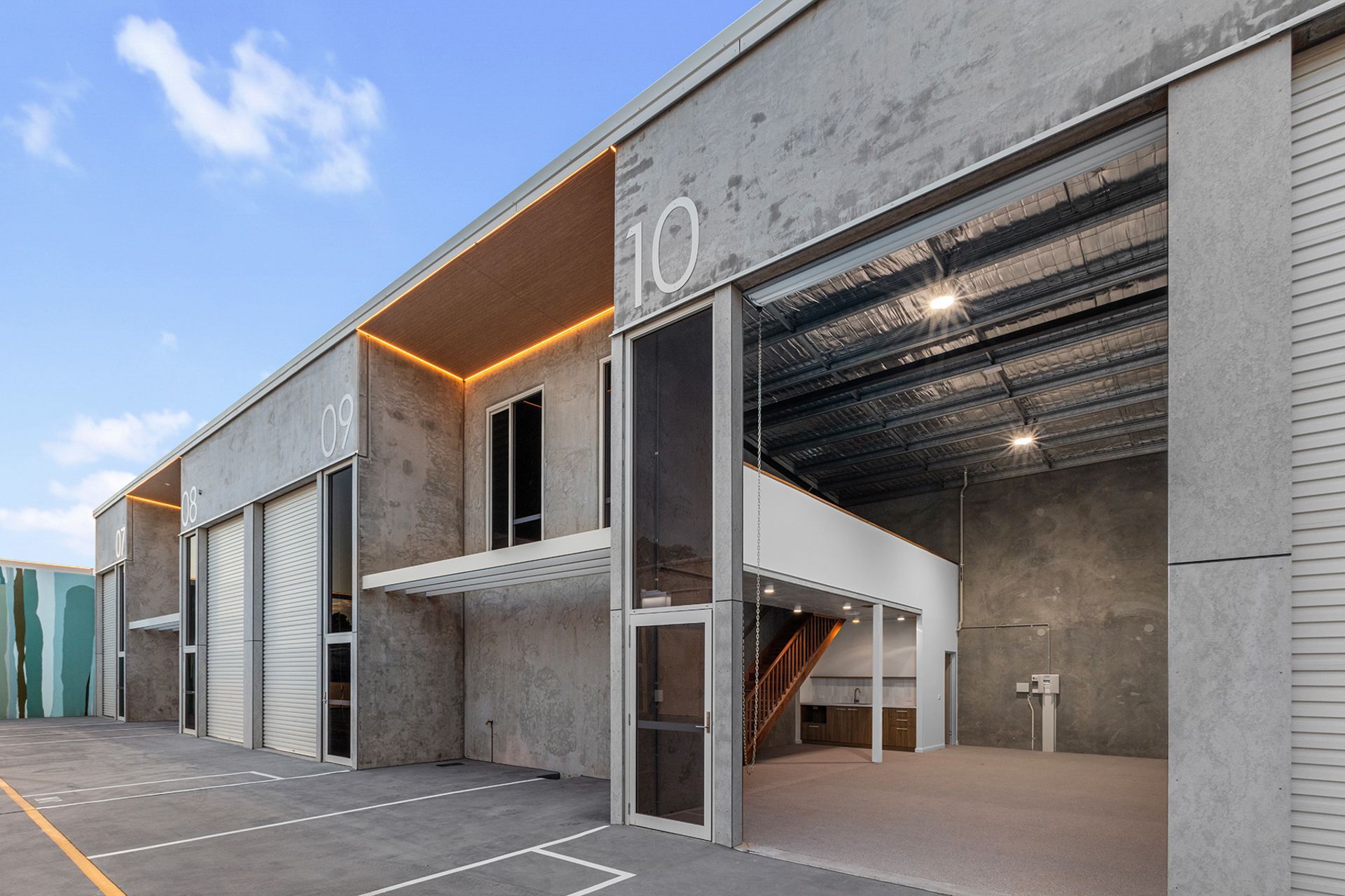 Exterior view of modern concrete industrial warehouse units with large roll-up doors under a bright blue sky.