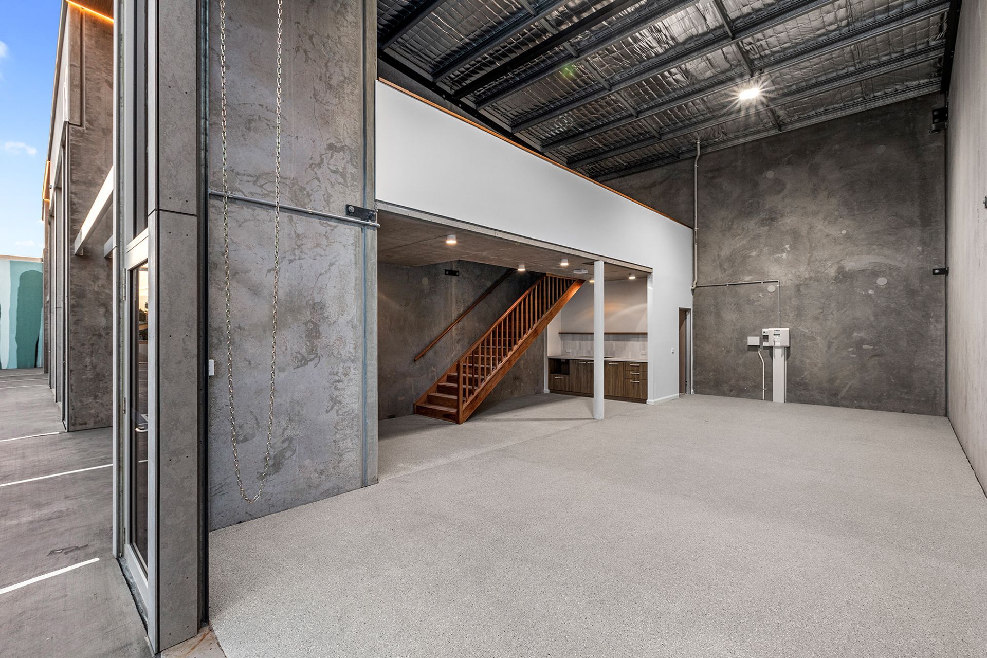 Industrial interior with gray concrete walls, a wooden staircase, and an open warehouse space under a metal roof.
