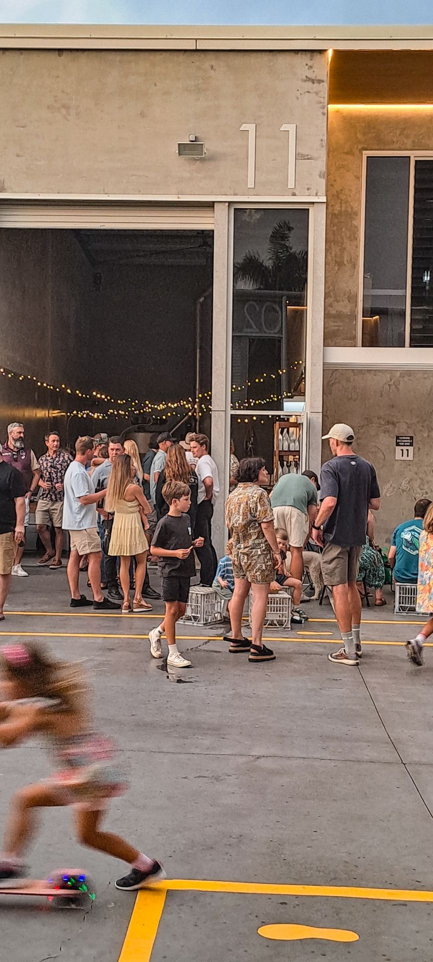 A blurred person skates past a group of people gathered outside a warehouse building marked with the number 11.