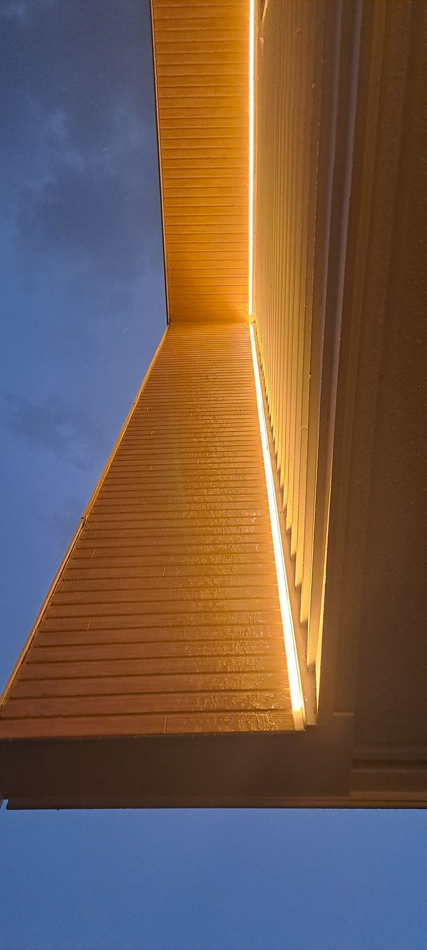 Low-angle view of a textured, light-colored wall illuminated by a vertical strip light against a twilight blue sky.