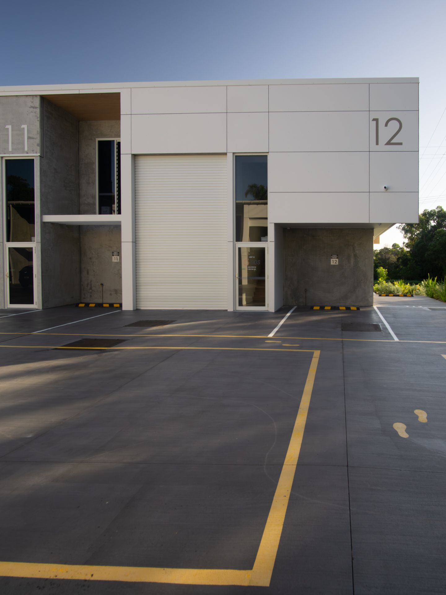 A modern commercial building with white panels, concrete walls, and large number labels 11 and 12, above a parking lot.
