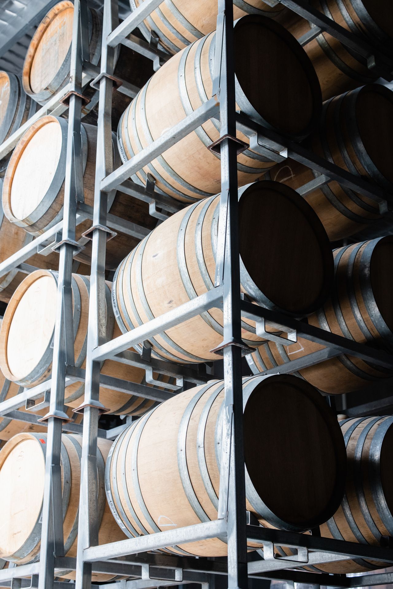Wooden barrels stacked in metal storage racks in a cellar.