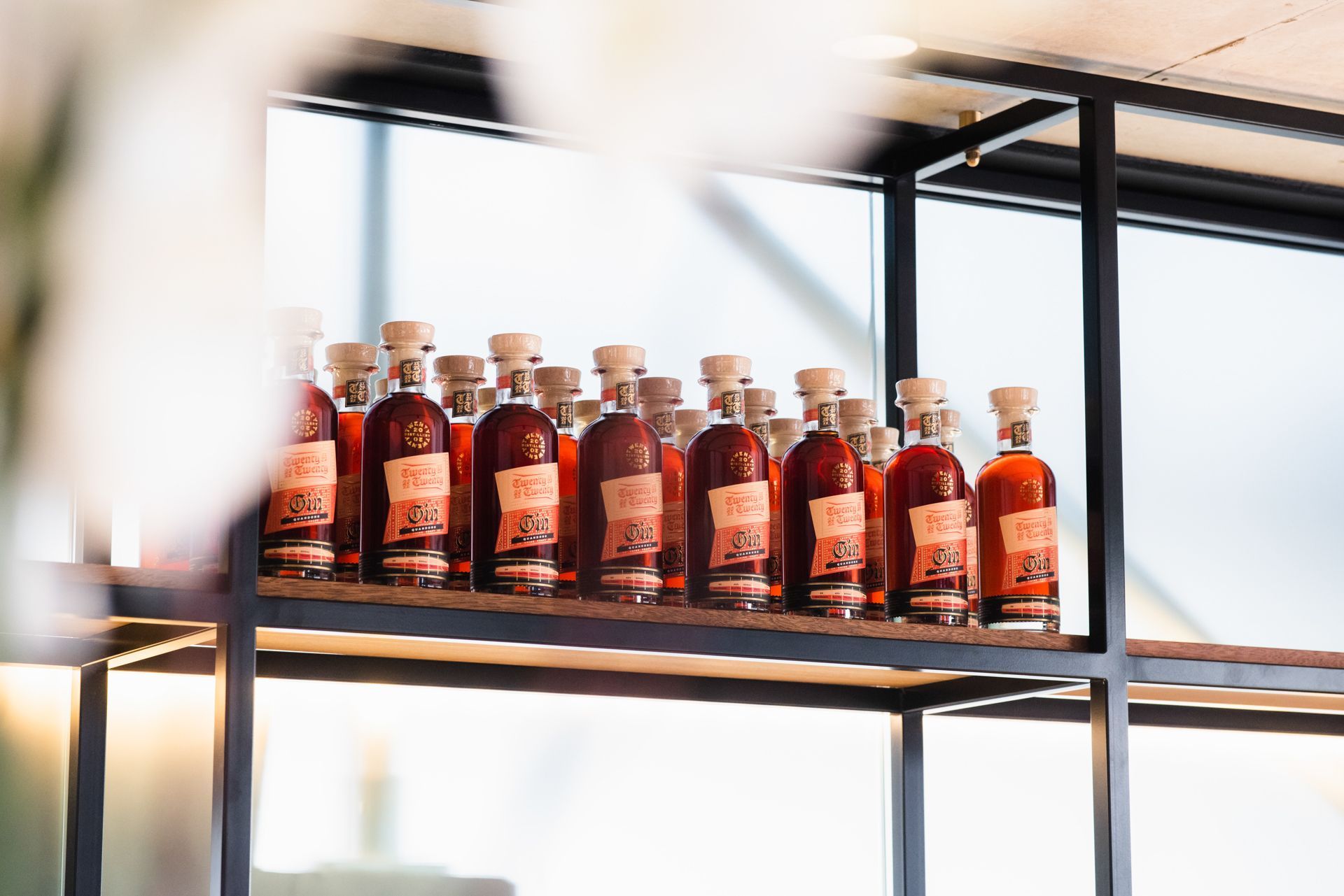 A row of identical small bottles with dark amber liquid and light-colored labels sitting on a modern black metal shelf.