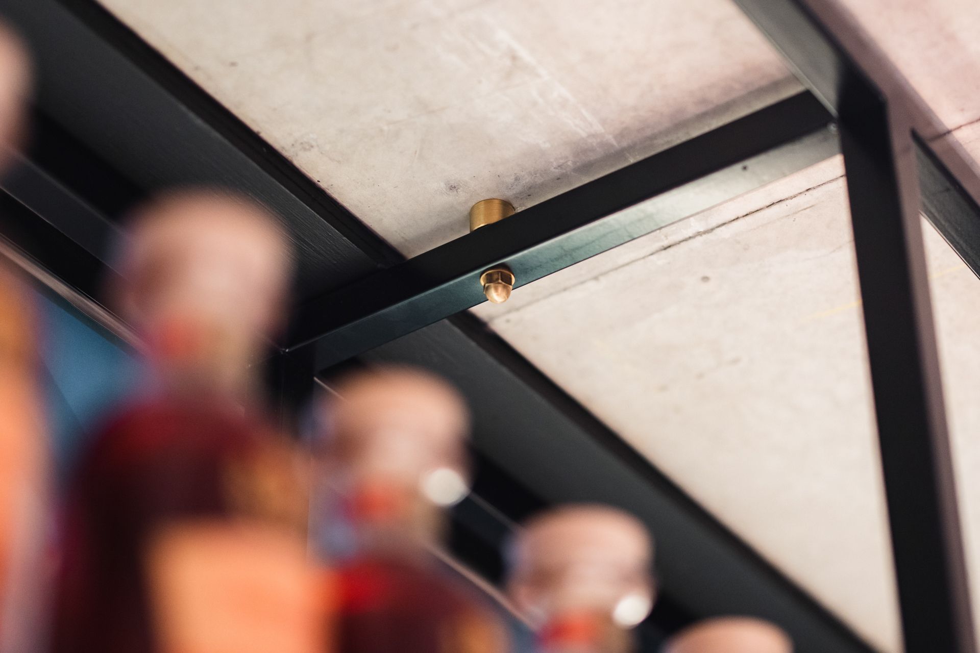 A metal ceiling fixture and black steel frame are visible above a blurred foreground of glass bottles.