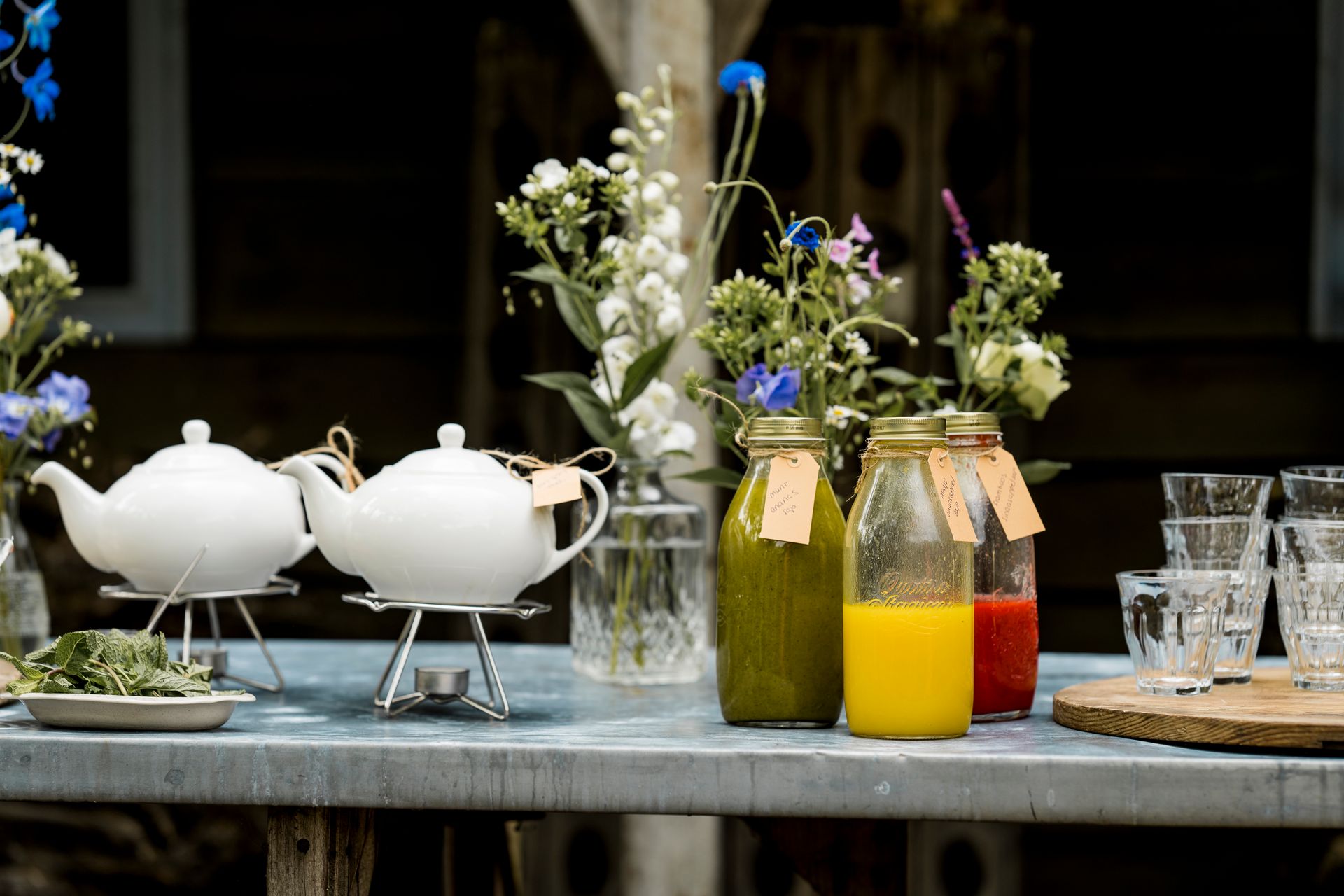 Tafel met theepotten, sapflessen, bloemen en glazen.