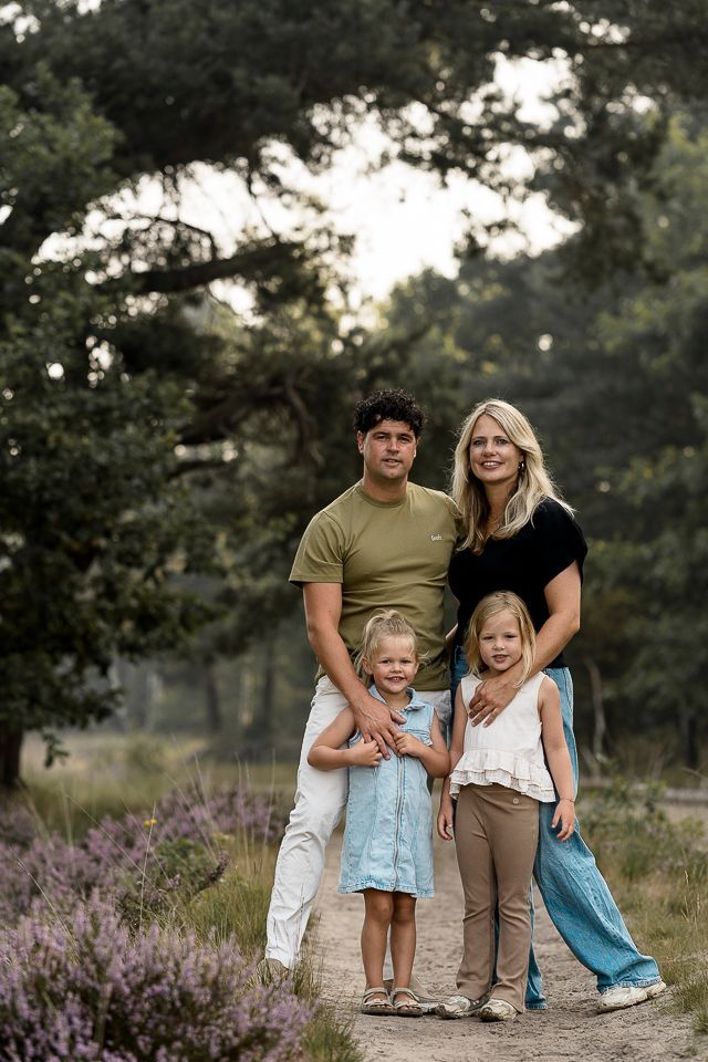 Een gezin van vier staat op een pad in een bos; ouders en twee jonge kinderen.