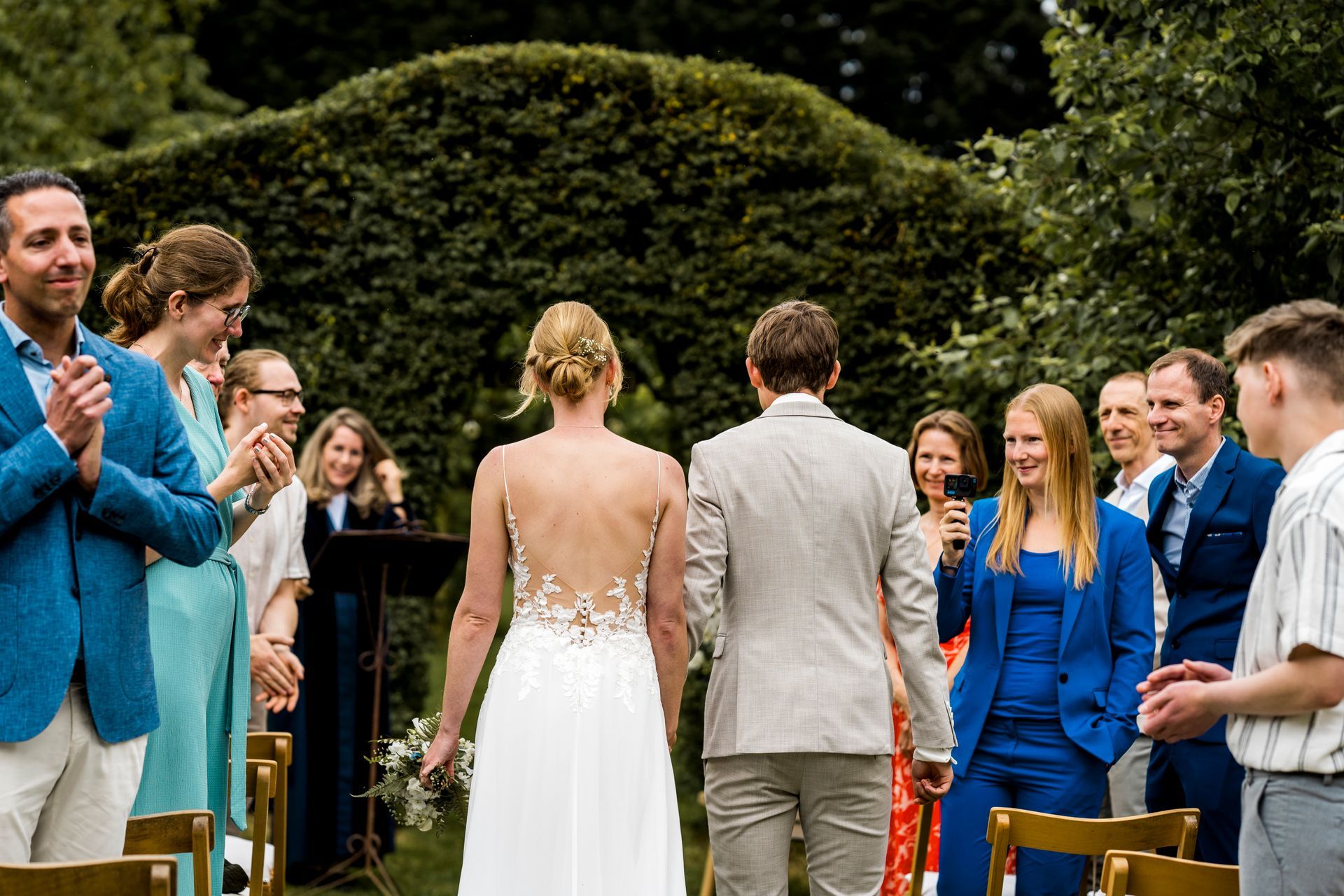 Na de huwelijksceremonie in een tuin lopen de bruid en bruidegroom hand in hand naar de gasten toe.
