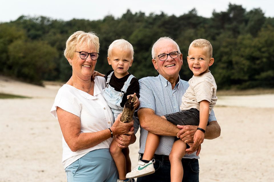 Grootouders met twee lachende jonge kinderen in een lichte buitenomgeving.