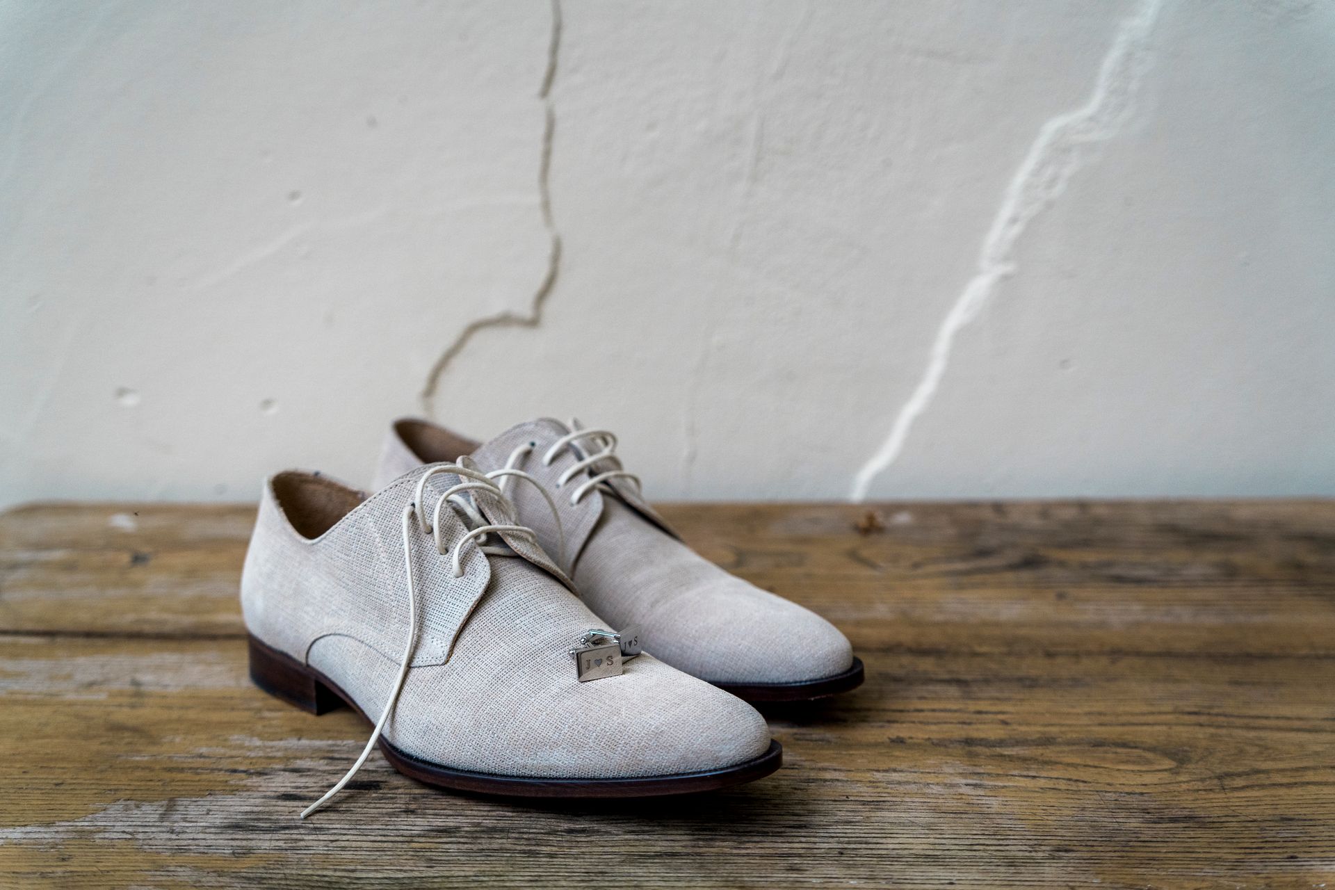 Witte suède geklede schoenen op een houten ondergrond, met een muur met structuur op de achtergrond.