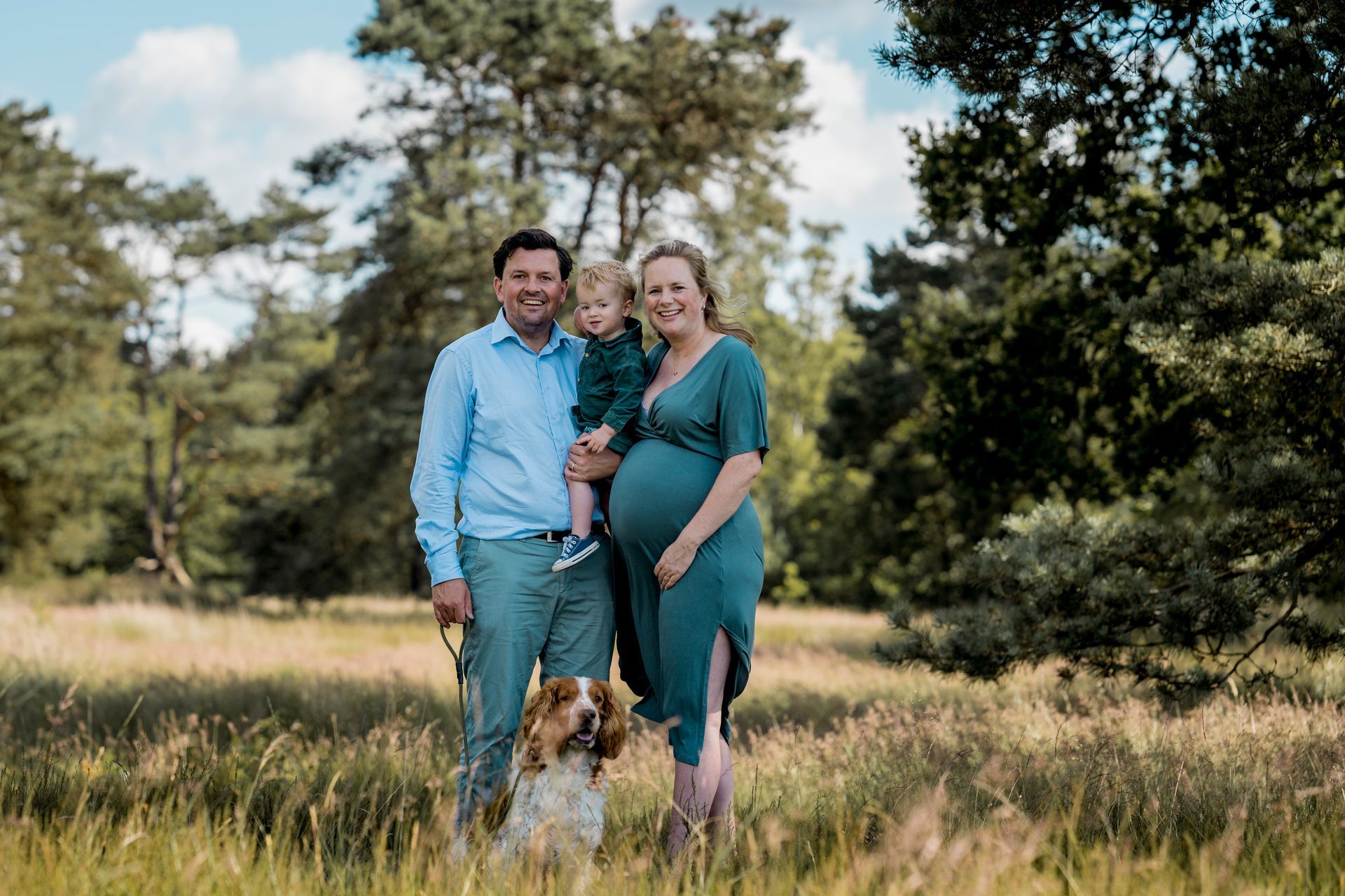 Een gezin met een zwangere vrouw en kind poseert in een weiland met een hond.