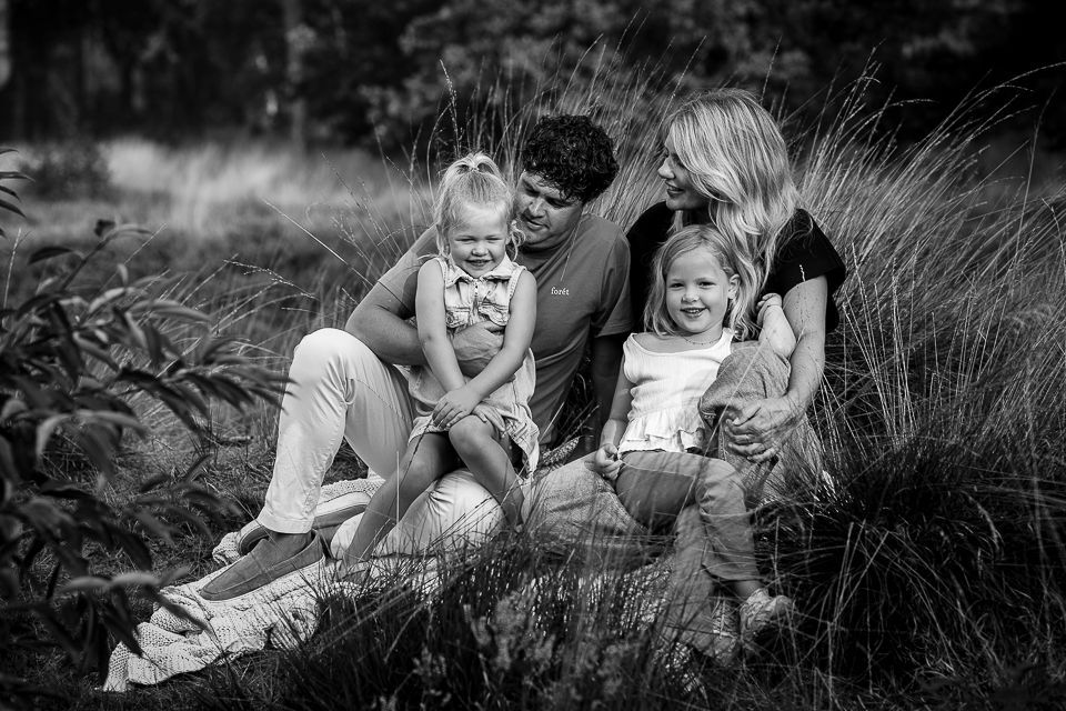 Een gezin van vier zit lachend in het hoge gras. Zwart-witfoto.