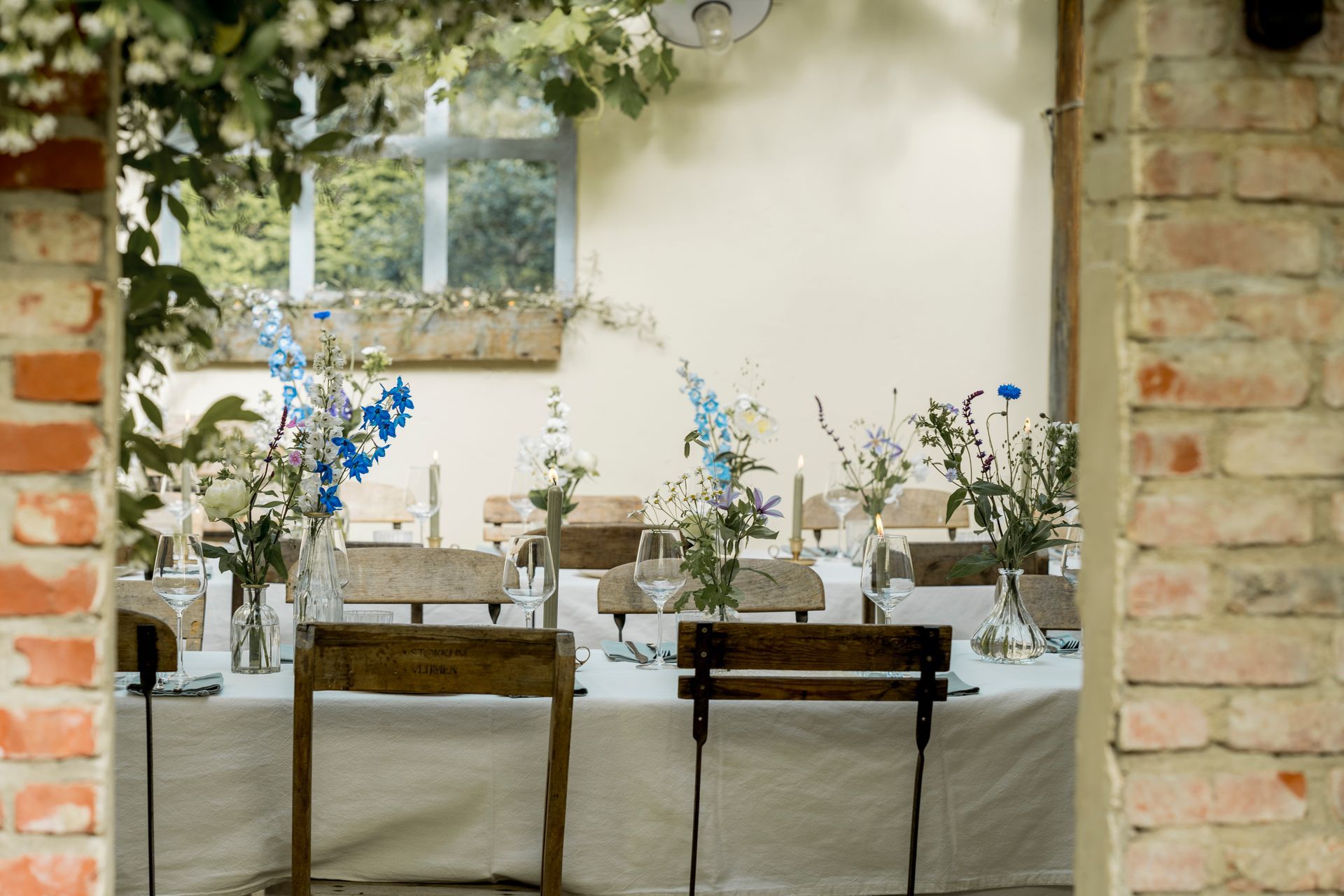 Zicht op een gedekte tafel door een bakstenen boog; bloemen en kaarsen op de tafel.