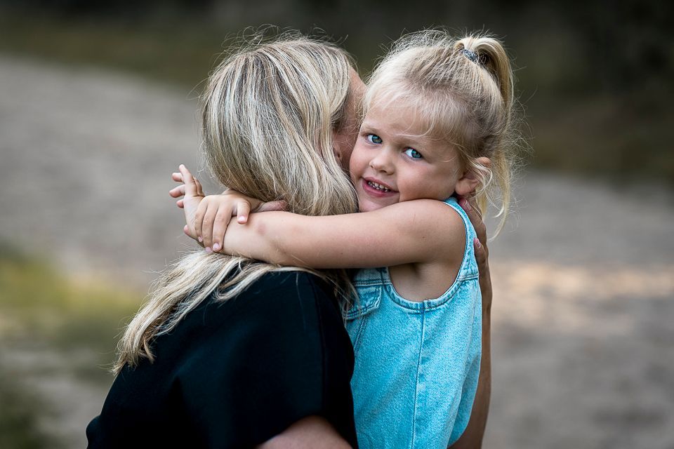 Vrouw omhelst een lachend kind met blond haar in de buitenlucht.