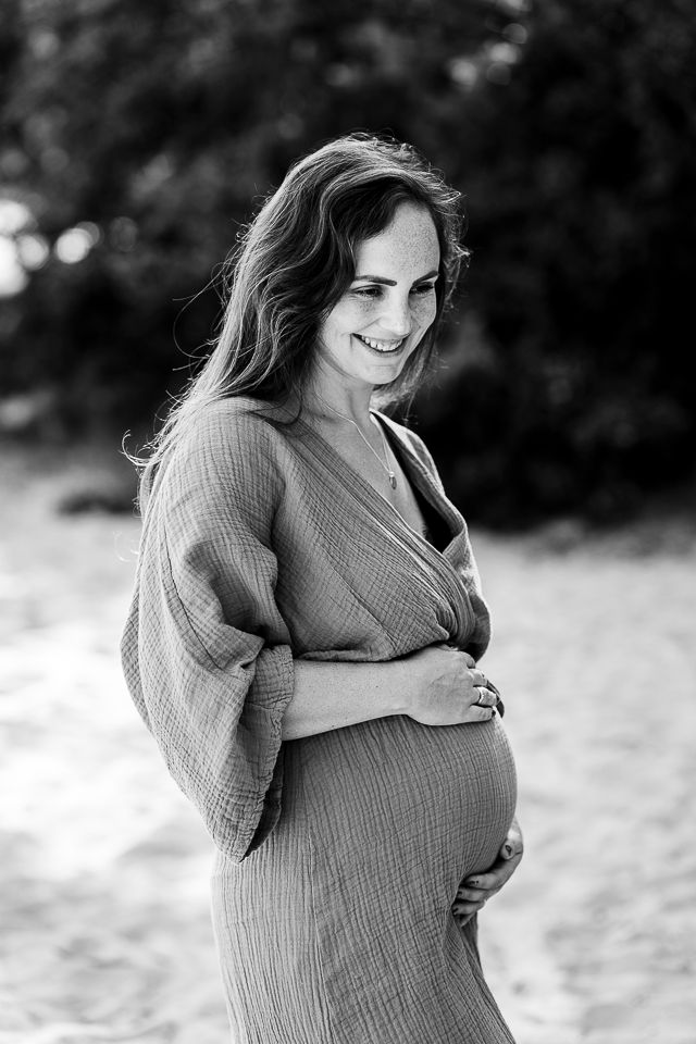 Een zwangere vrouw lacht buiten en houdt haar buik vast. Zwart-witfoto.