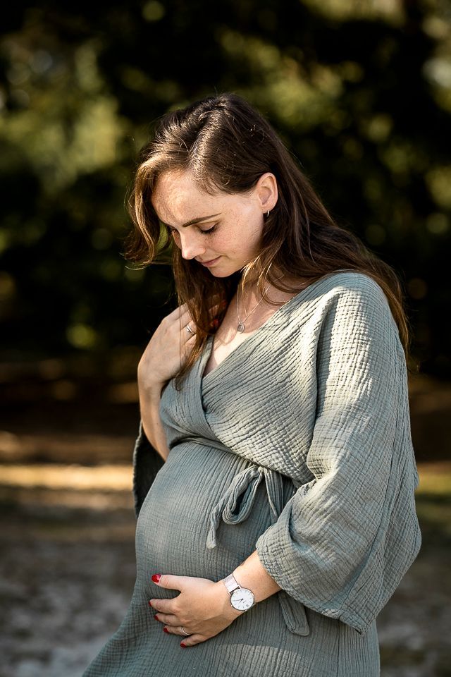 Zwangere vrouw in saliegroene ochtendjas, raakt haar buik aan, buiten.