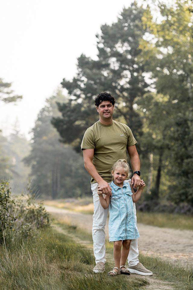 Een man en een jong kind staan ​​hand in hand op een pad in een bos.