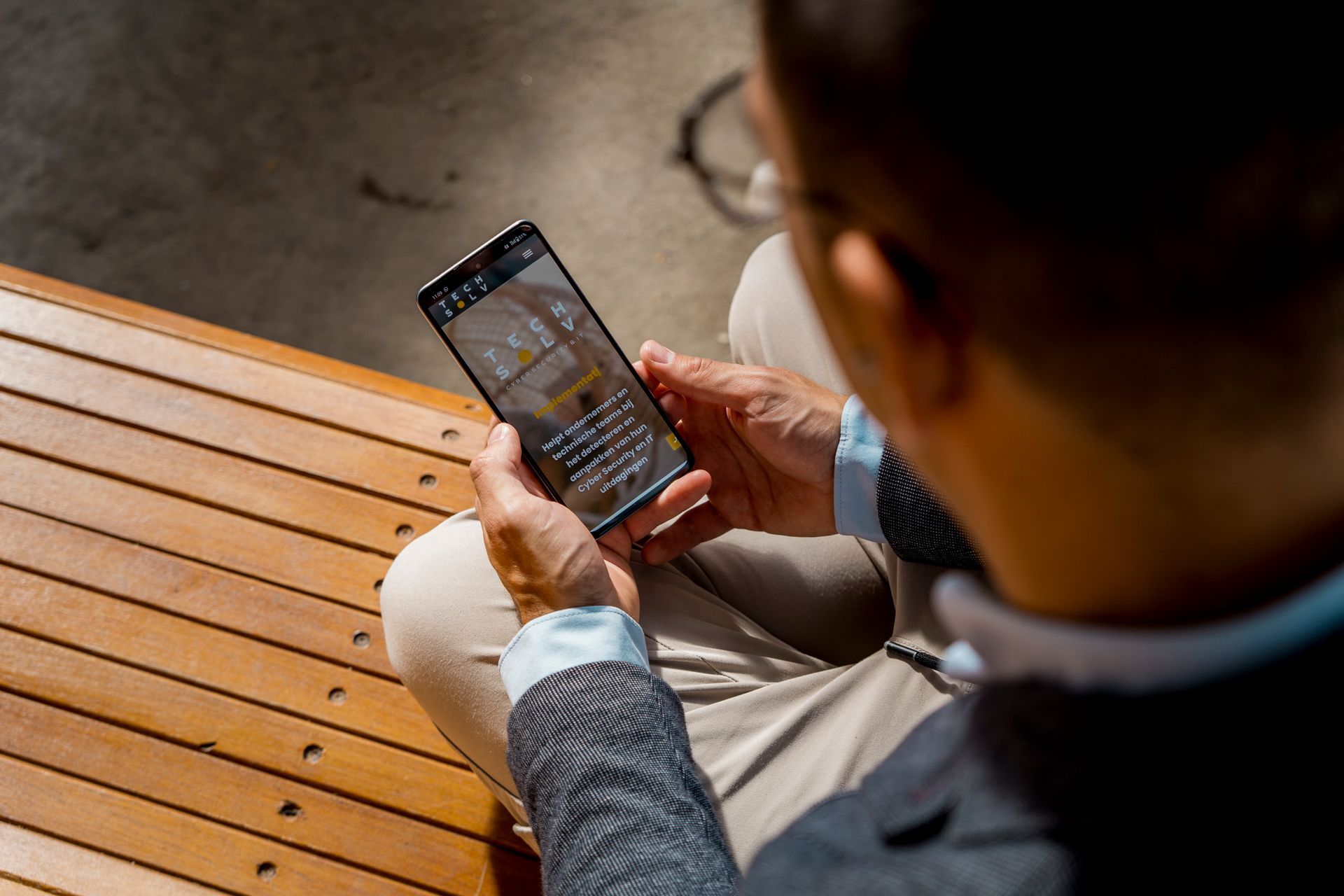 Een man zit op een houten bank en kijkt naar zijn smartphone.