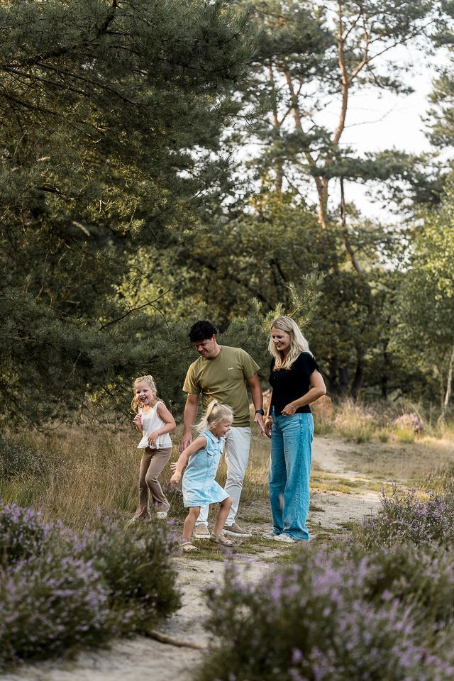 Een gezin wandelt over een pad omgeven door bomen en paarse bloemen.