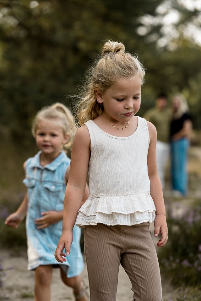 Twee jonge meisjes lopen buiten, de ene in een witte top en een bruine broek, de andere in een blauwe jurk.