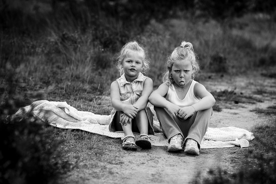 Twee kinderen zitten buiten en kijken naar de camera. Ze dragen casual kleding. Zwart-wit.