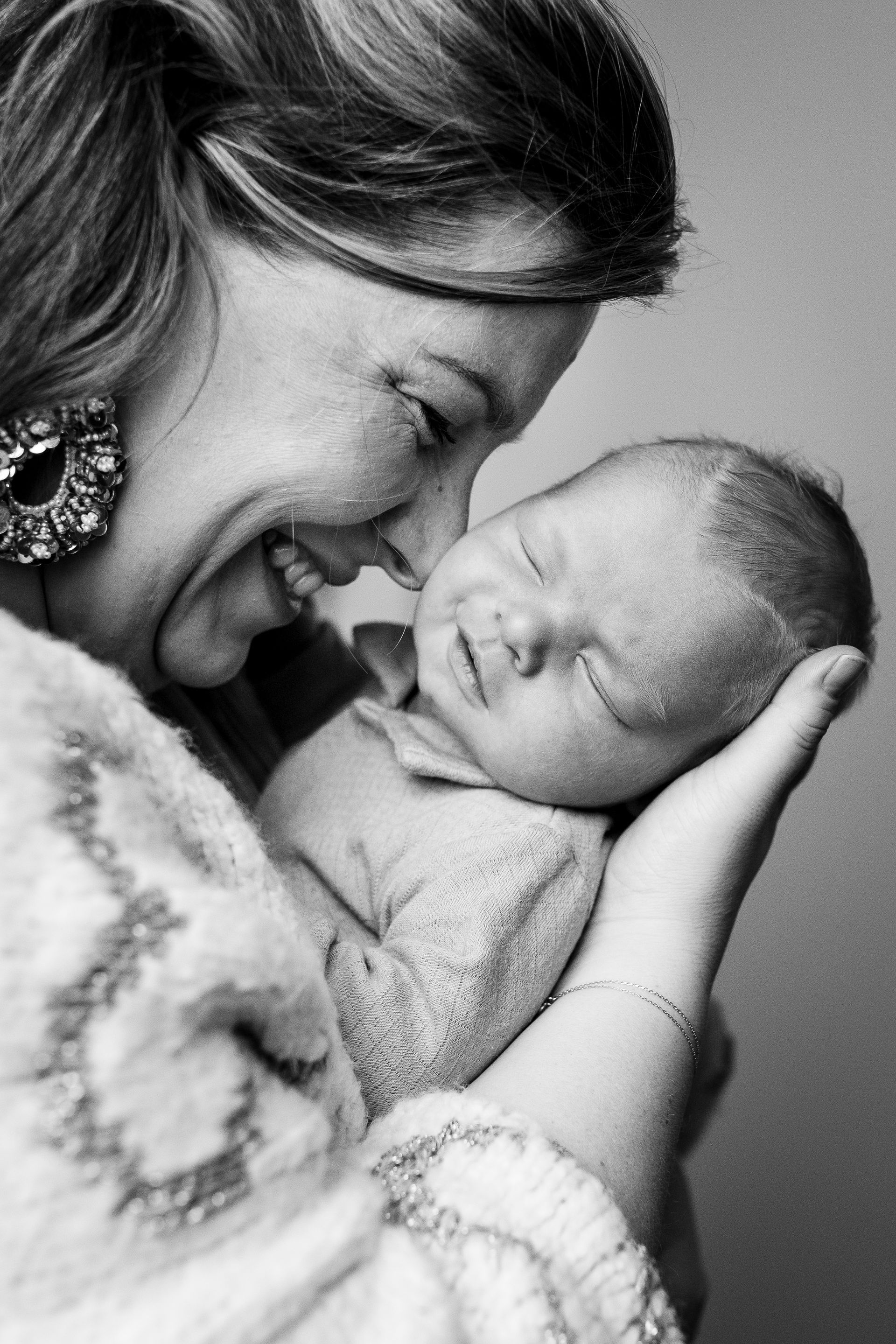 Vrouw lacht en houdt een slapende baby dicht tegen zich aan. Zwart-witfoto.