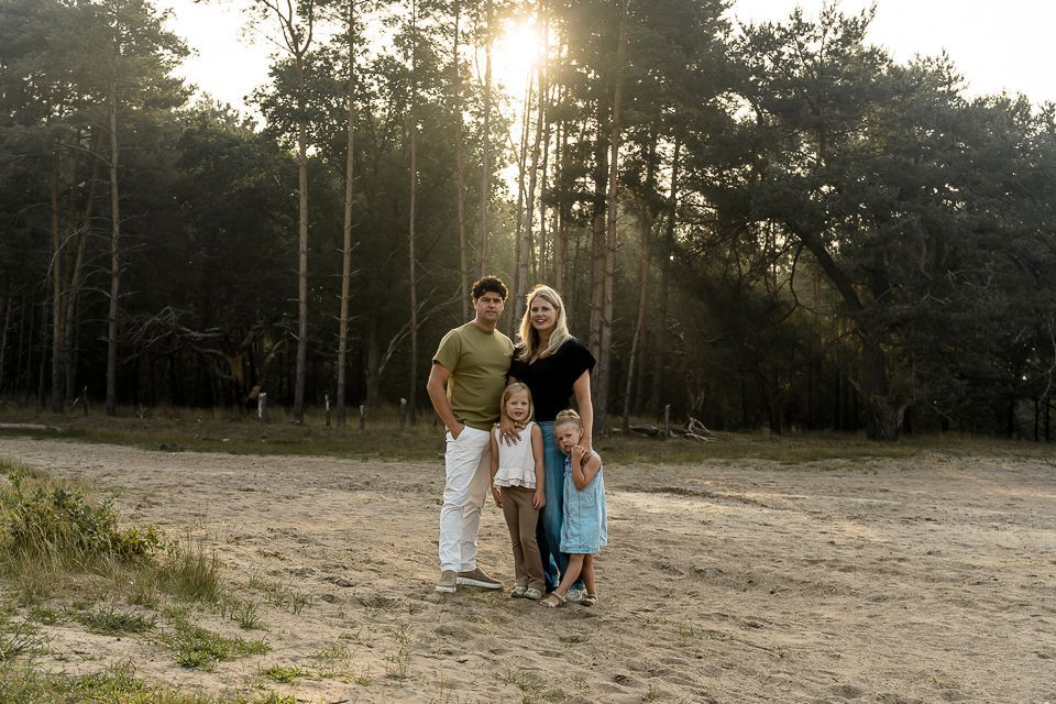 Een gezin van vier staat in een bos, de zon schijnt door de bomen.