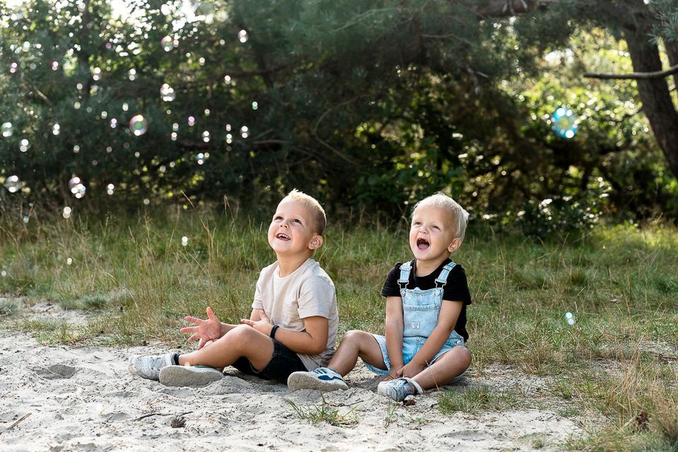 Twee jonge kinderen zitten in een grasveld en kijken naar de bubbels.