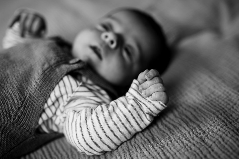 Zwart-witfoto van een pasgeboren baby die op een deken ligt, met de armen omhoog, een gestreept shirtje draagt en lijkt te slapen.