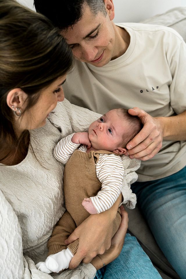 Ouders wiegen een pasgeboren baby in hun armen en kijken allemaal naar het kindje.