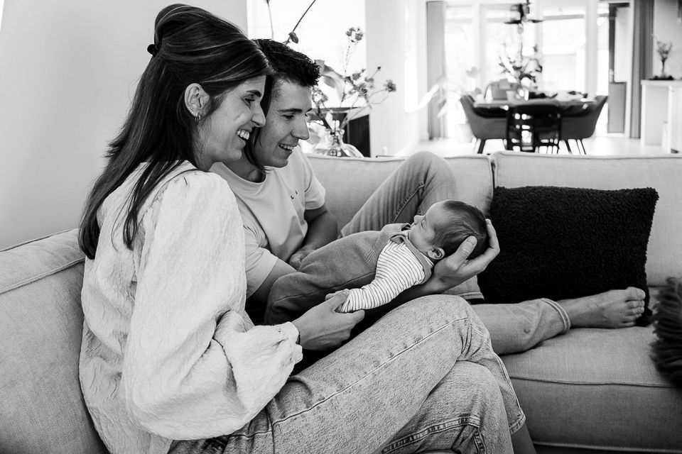 Ouders glimlachen terwijl ze een pasgeboren baby vasthouden op een bank. Woonkamer.