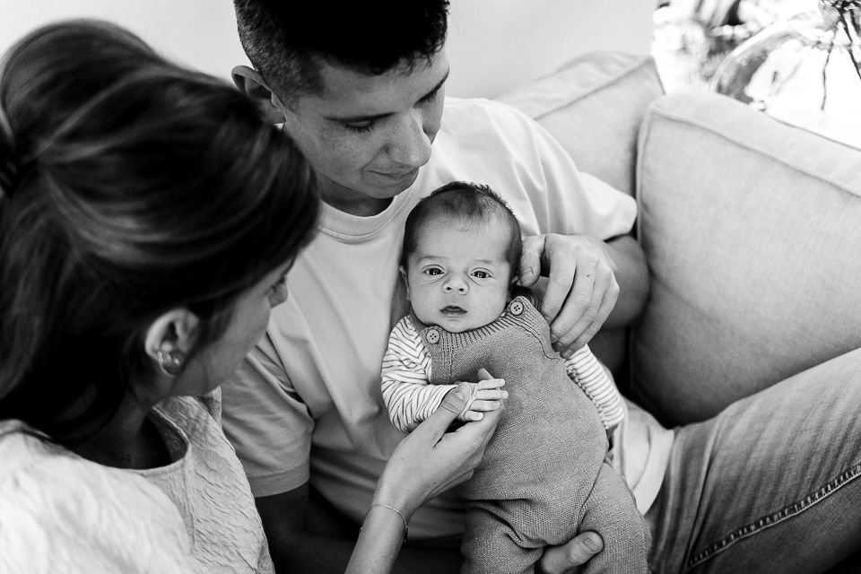 Ouders houden een pasgeboren baby vast op een bank en kijken naar de baby. Zwart-wit.