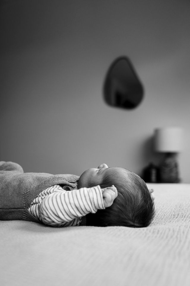 Baby ligt op een bed, zijprofiel. Draagt een gestreepte pyjama, met een wazige muur en lamp op de achtergrond.