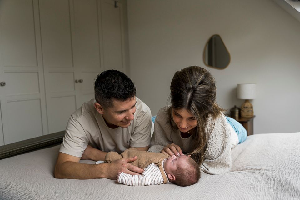 Ouders kijken vol bewondering naar hun pasgeboren baby die op een bed ligt.