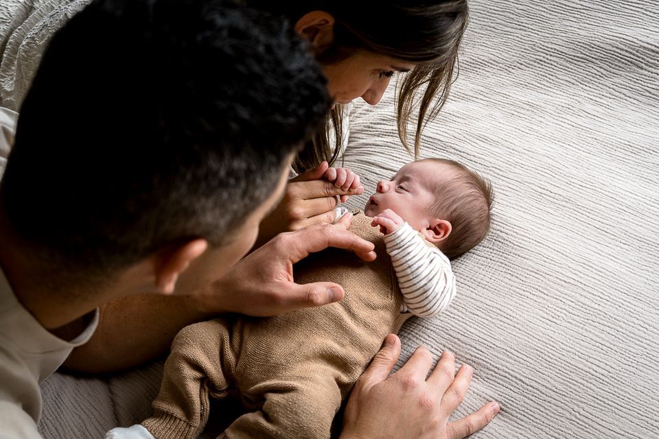 Gezin met pasgeborene: ouders en kind op bed, kijkend naar de baby.