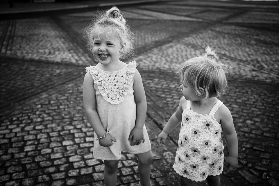 Twee jonge kinderen op de kinderkopjes; de ene steekt zijn tong uit, de andere kijkt toe.